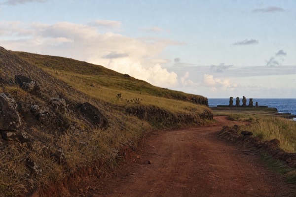 Empty coastal road on Easter Island winding past volcanic slopes toward a distant ahu platform