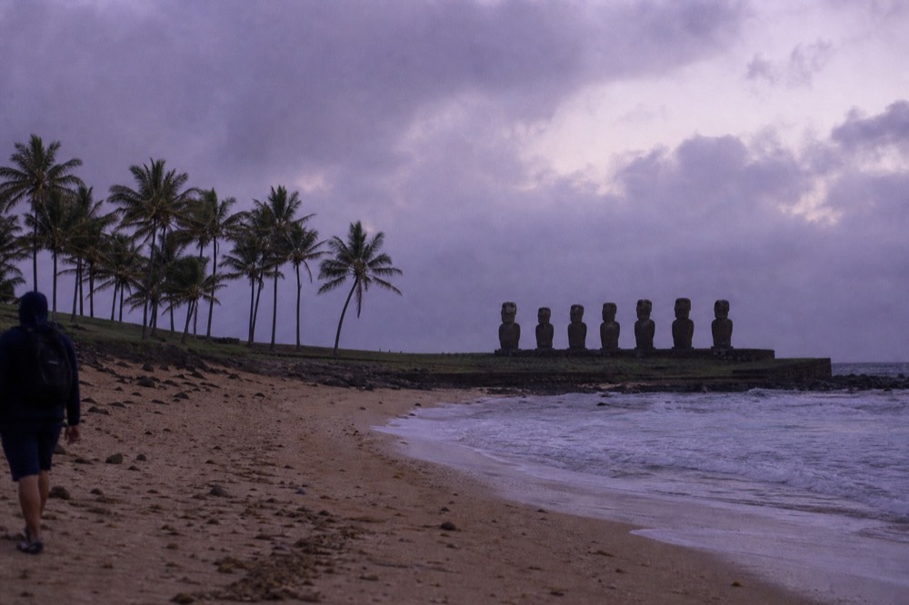 Pale coral sand beach backed by palms with a row of moai on a stone platform at the far end
