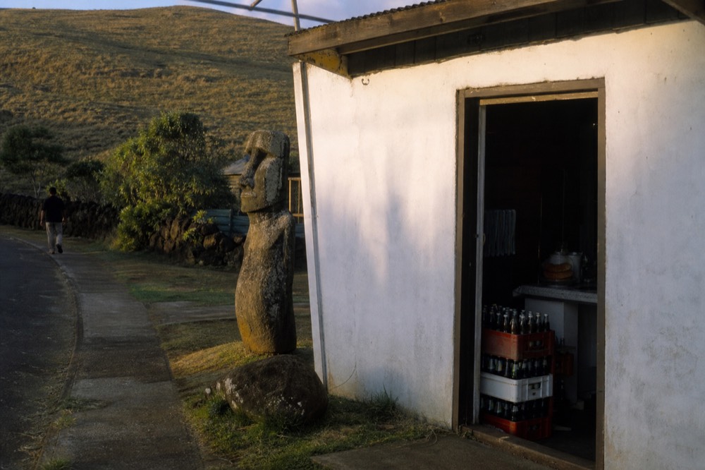 Small whitewashed shopfront on a quiet Hanga Roa street with crates of bottled drinks stacked outside the doorway