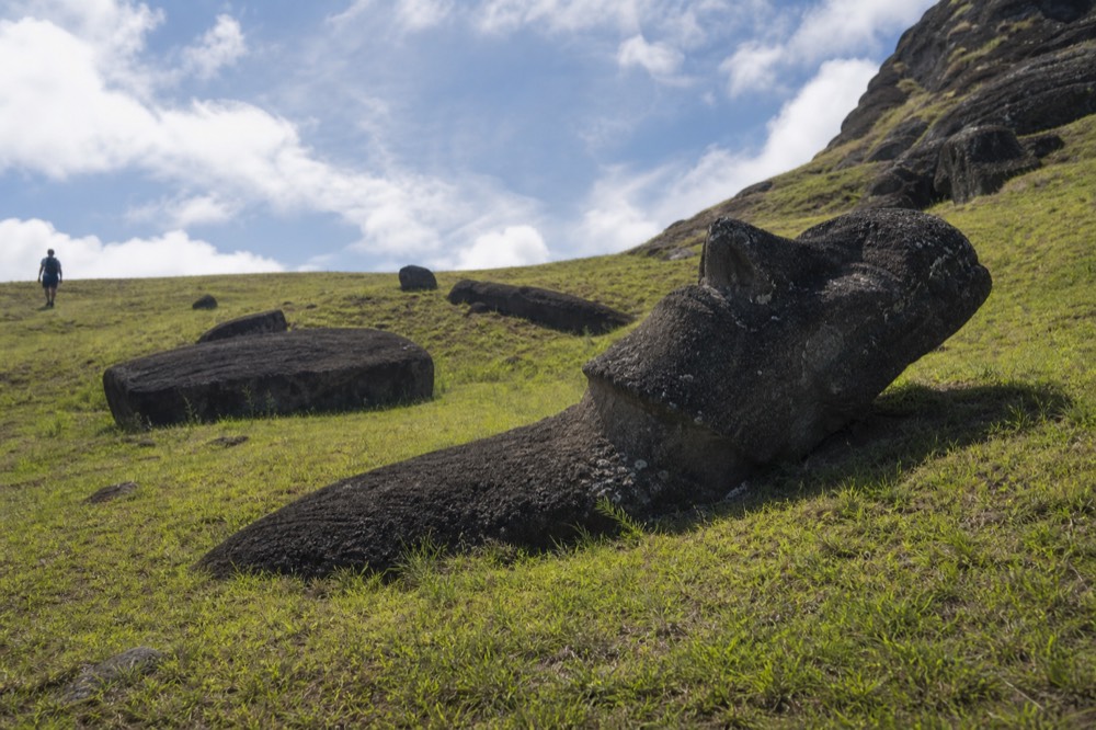 Treeless green slope of the Rano Raraku quarry in hard midday sun with unfinished moai lying in the grass