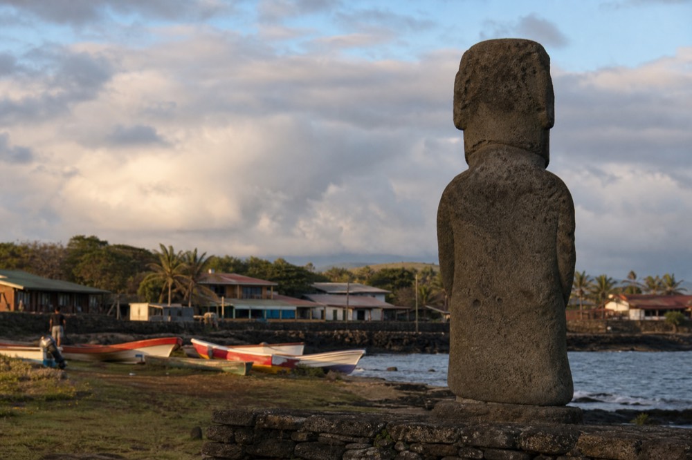 Low-slung guesthouses and painted fishing boats along the small harbour at Hanga Roa under scattered afternoon cloud