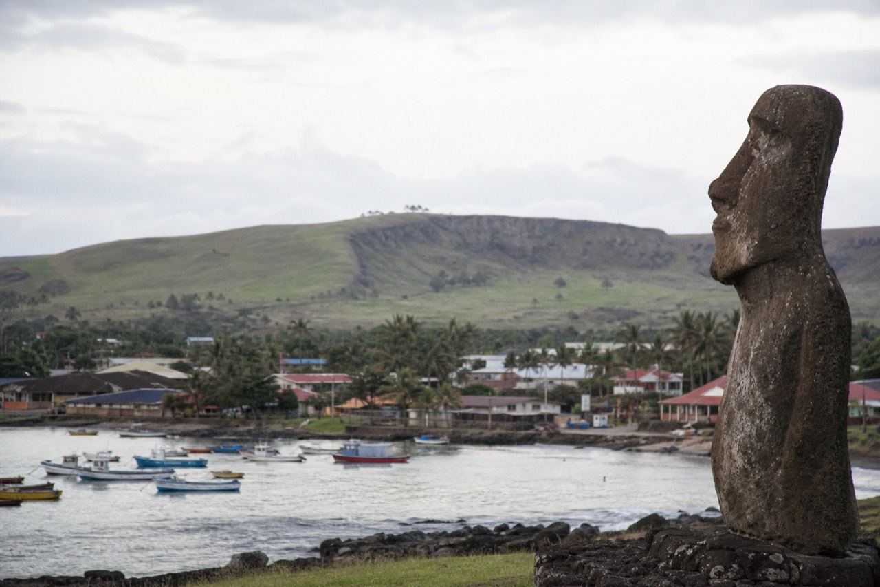 Small fishing boats moored in the harbour at Hanga Roa with low painted houses and palms rising behind