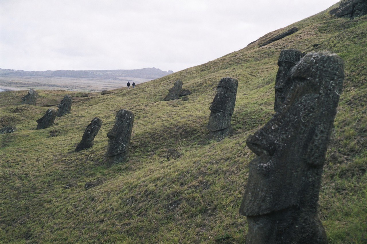Dozens of partly buried moai scattered at different angles across a green volcanic quarry slope