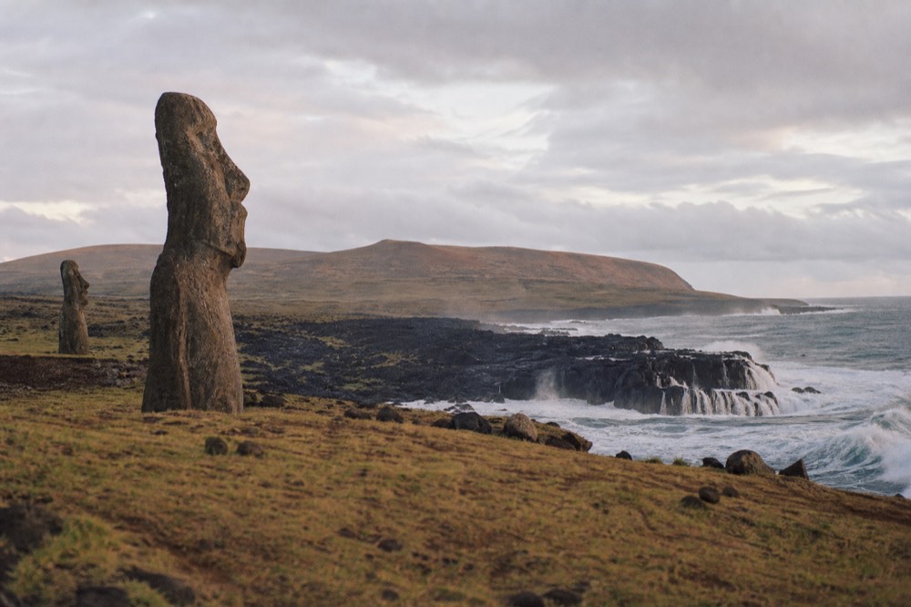 Waves breaking hard against black volcanic rock along an exposed stretch of the south coast under a grey windy sky