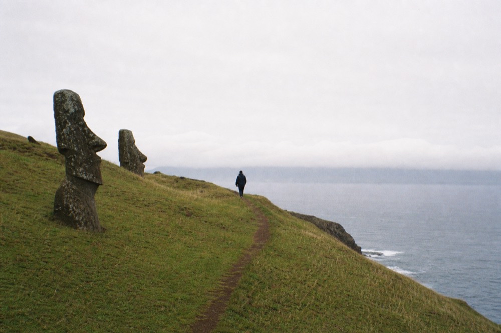 Narrow marked footpath running along a grassy ridge above a steep drop to the ocean with low cloud on the horizon