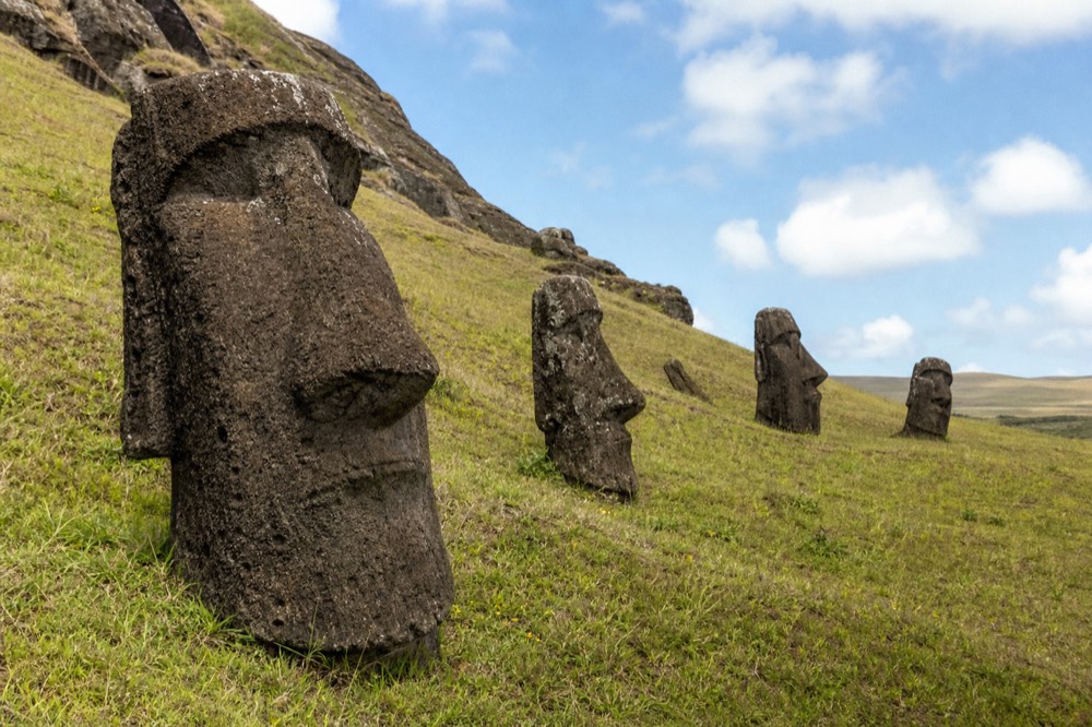 Half-buried moai heads tilted at different angles across the grassy outer slope of the Rano Raraku quarry