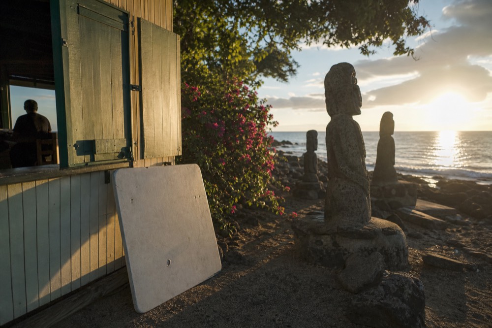 Handwritten price board propped outside a small island eatery with painted wooden shutters and bougainvillea behind