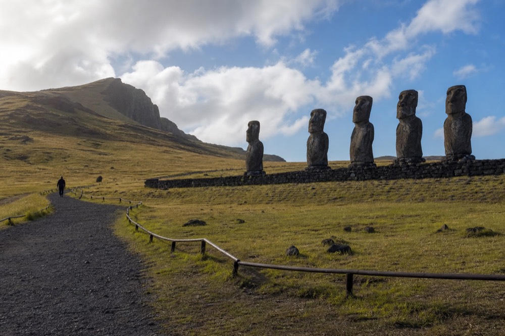 Marked gravel path curving past a roped-off stone platform with several moai standing beyond it