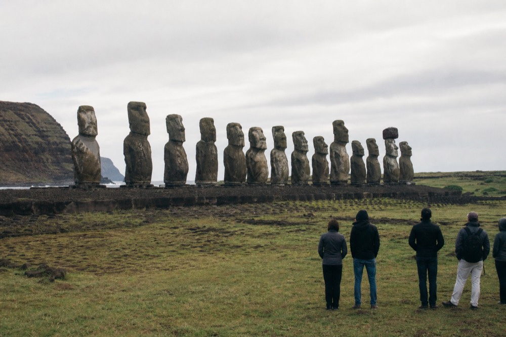 Small group standing on open ceremonial ground at a respectful distance in front of a line of moai