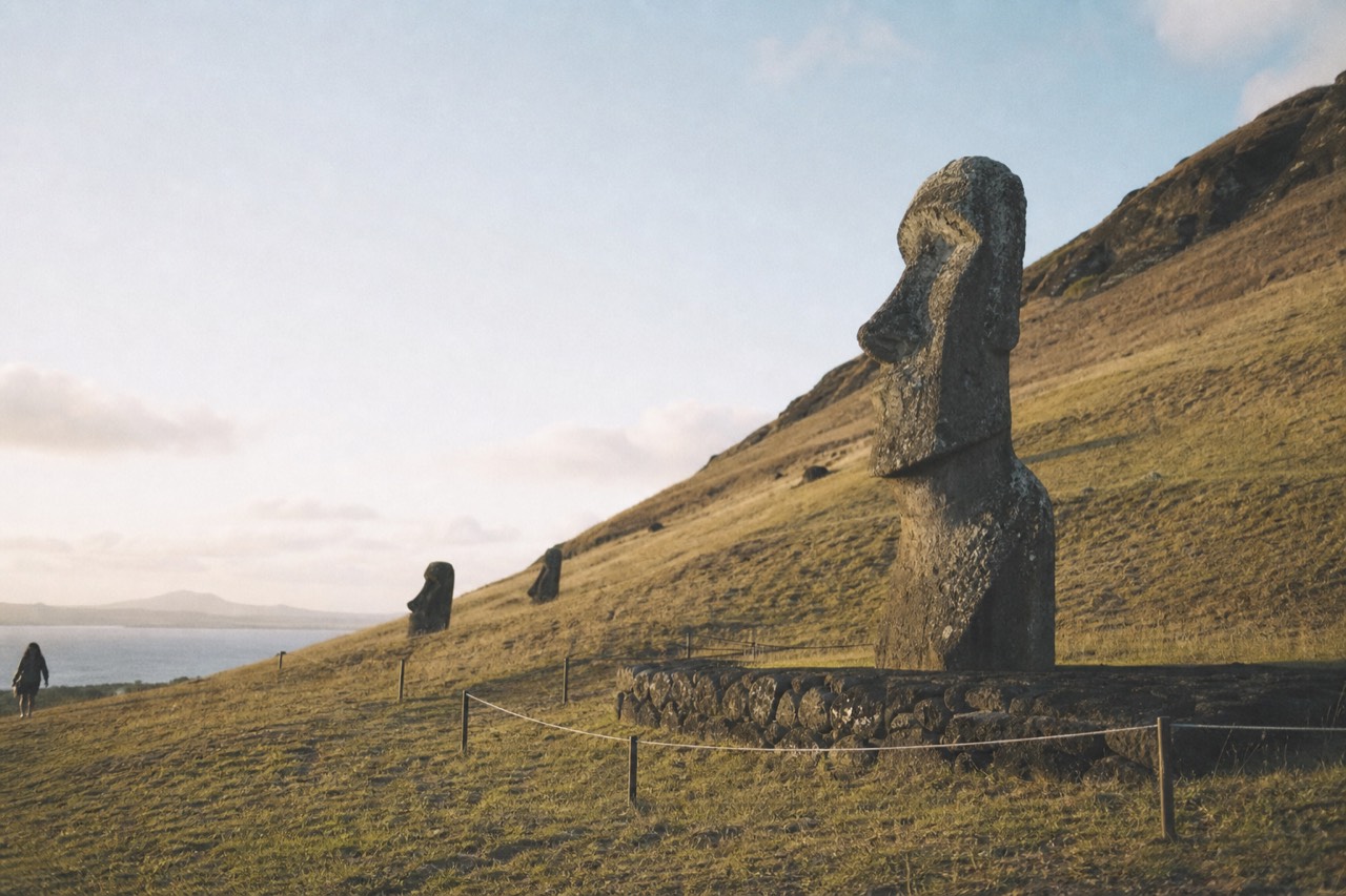 Low rope barrier staked into grass a few metres in front of a weathered stone moai on its platform