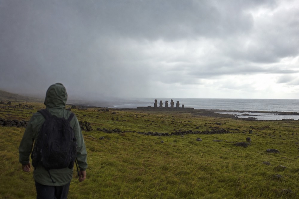 Grey rain squall crossing green pasture towards a lone stone ahu on the island's rocky southern shoreline