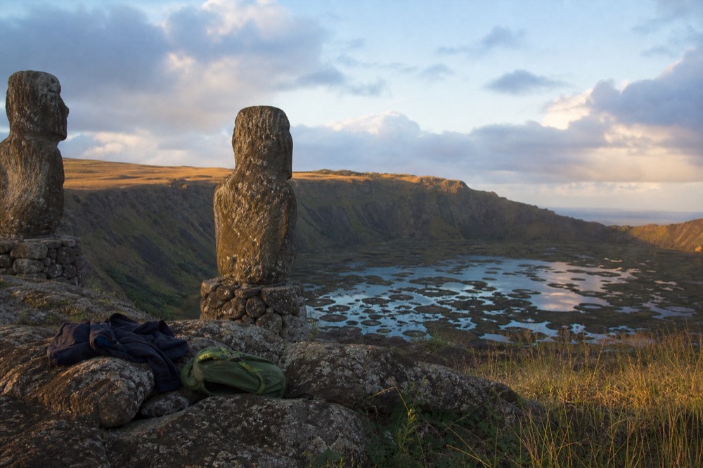 Windbreaker jacket and small daypack resting on a rock ledge above the flooded green crater of Rano Kau