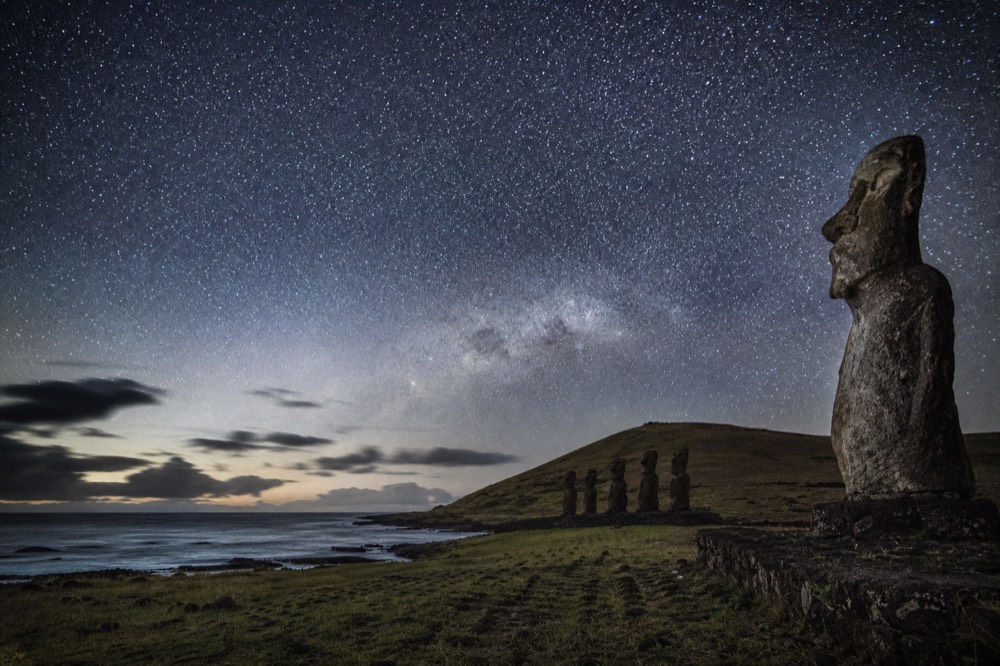 Dense southern night sky and the Milky Way arching over a dark grass headland above the Pacific