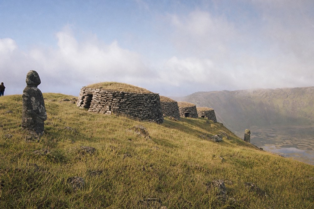 Restored stone houses of the Orongo ceremonial village perched on the narrow rim above the Rano Kau crater lake