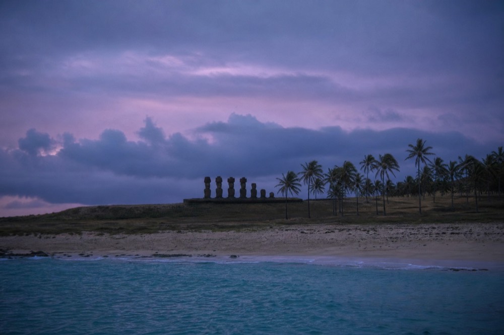 Turquoise water and coral sand at Anakena with the moai of Ahu Nau Nau standing behind the palm line