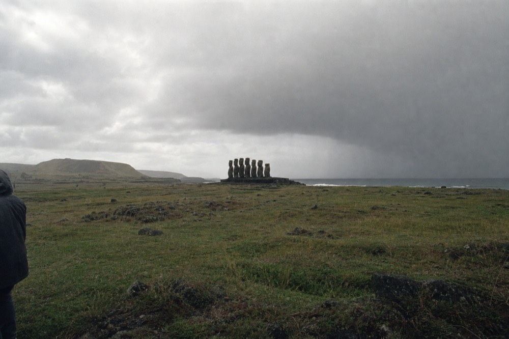 Rain squall sweeping across open volcanic grassland with a stone platform just visible in the distance