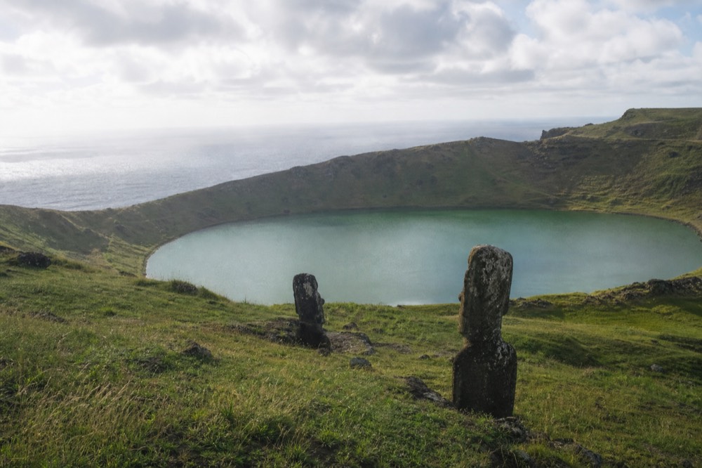 Wide green crater lake ringed by steep grassy walls under broken cloud on the island's southwest headland