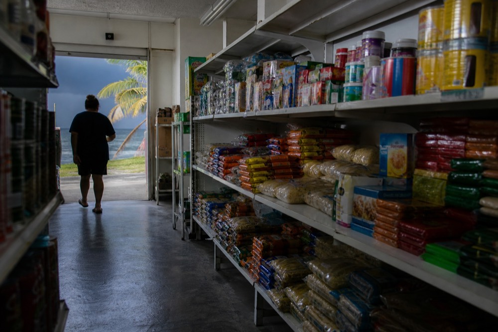 Small island supermarket aisle with imported packaged goods stacked on sparse shelves under fluorescent light