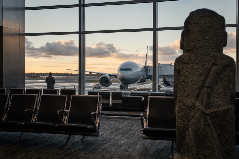 Empty departure gate at dawn with a wide-body aircraft visible through the window on the stand
