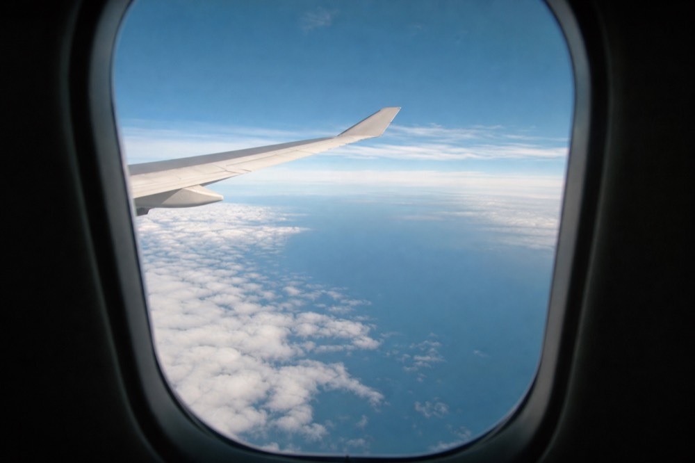 View through an aircraft cabin window of unbroken deep-blue Pacific ocean with high scattered cloud below the wing