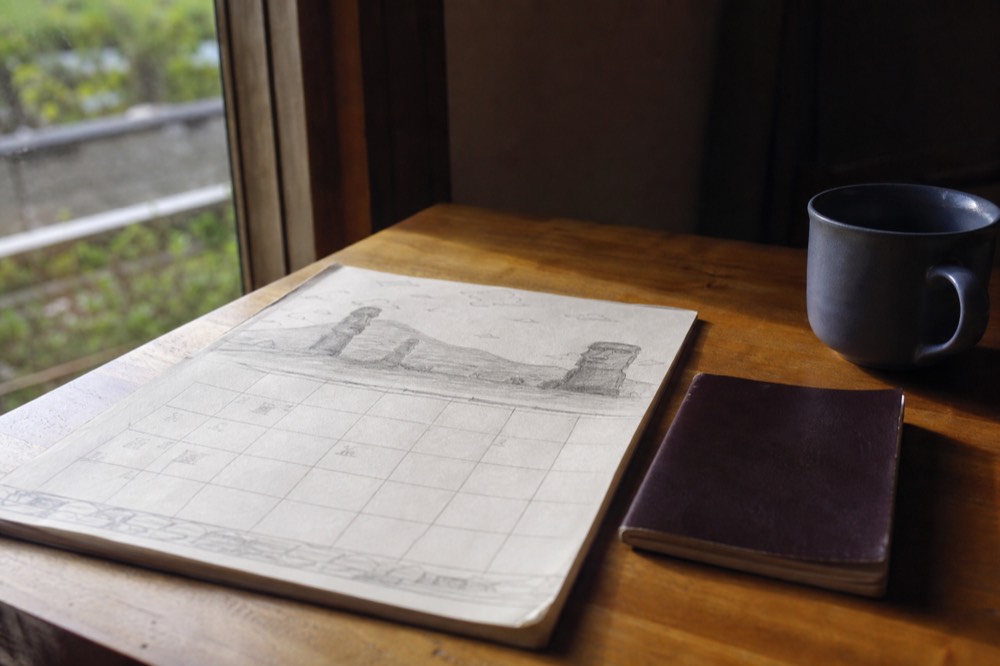 Hand-drawn calendar page on a wooden desk beside a passport and a coffee cup in soft morning light
