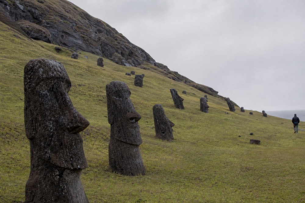 Quarry slope scattered with dozens of partly buried moai at different angles beneath a low grey sky