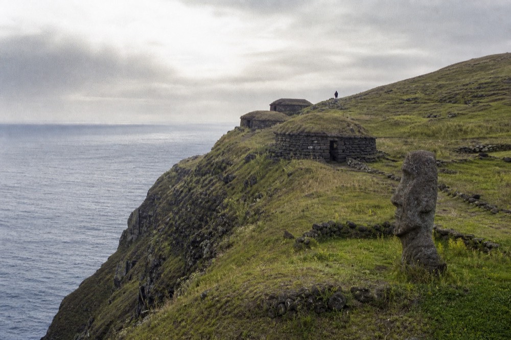 Low oval stone houses with turf roofs at Orongo clinging to a narrow ridge above the sea cliffs