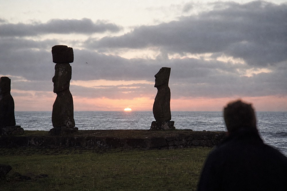 Moai at Tahai standing in dark silhouette as the sun drops into the Pacific behind low cloud