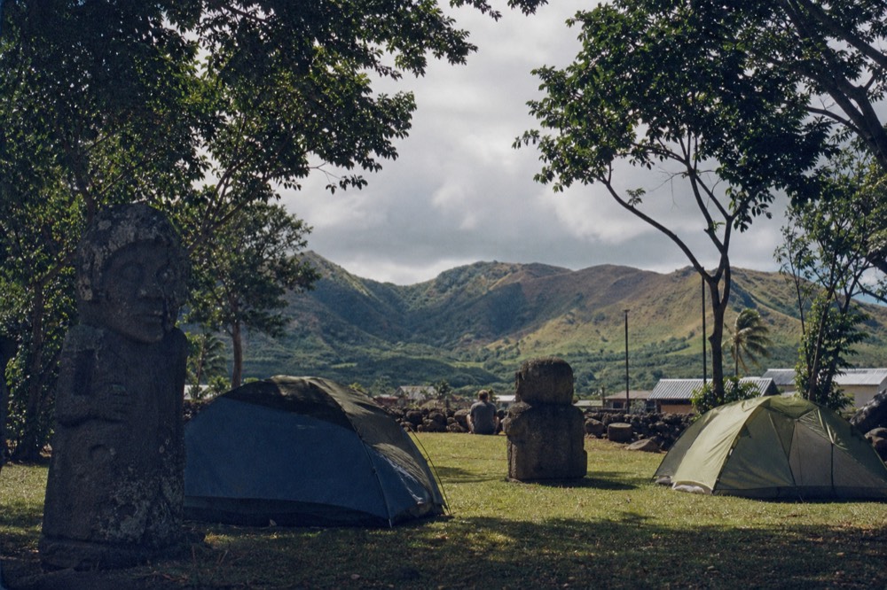Small tents pitched on mown grass under sheltering trees at a campsite on the edge of town