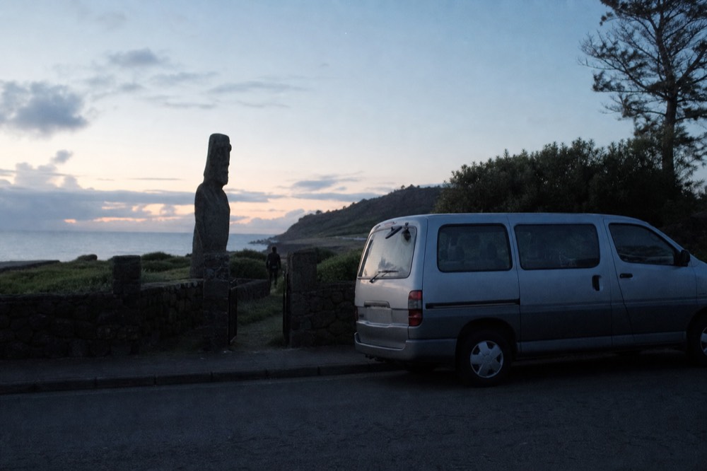Empty tour minivan waiting at the kerb outside a guesthouse gate in the pale light of early morning